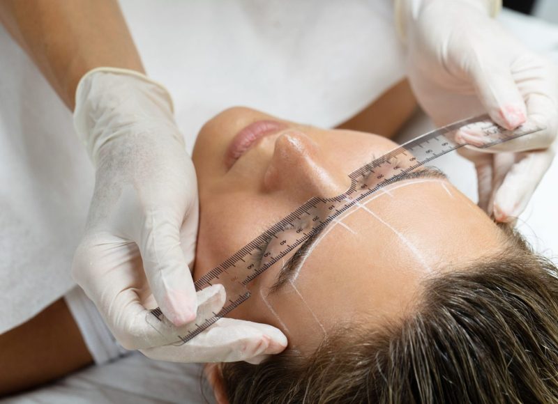 Young woman during professional eyebrow mapping procedure before permanent makeup